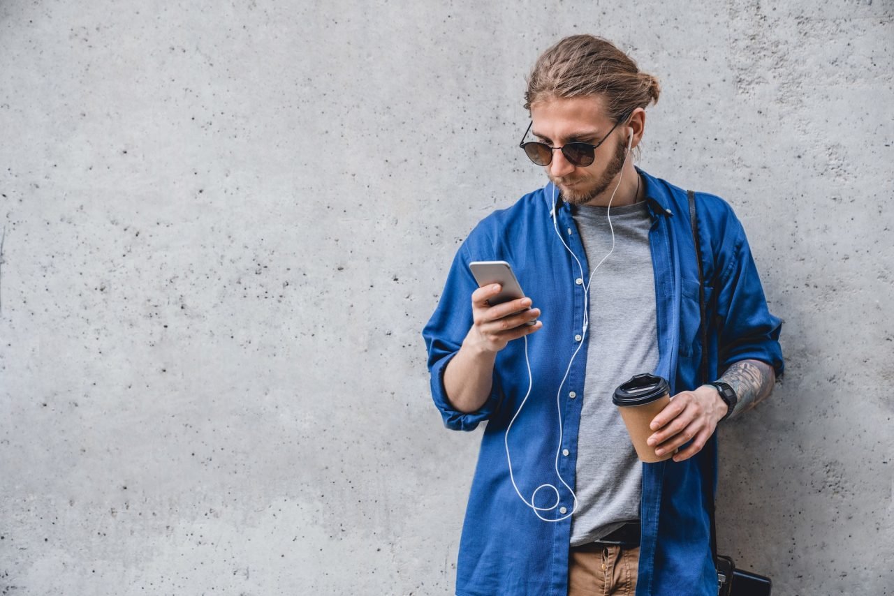 young-man-in-sunglasses-and-headphones-texting-message-on-smart-phone-isolated-on-grey.jpg